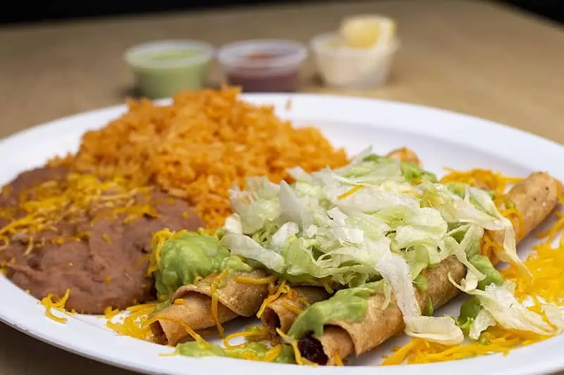 Flautas de res doradas servidas con lechuga, crema, queso y salsa mexicana