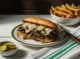 Plato con un Philly cheessteak con papas y pepinillos