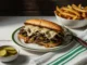 Plato con un Philly cheessteak con papas y pepinillos
