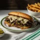 Plato con un Philly cheessteak con papas y pepinillos