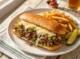 Plato con un Philly cheessteak con papas y pepinillos