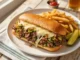 Philly Cheesesteak Sándwich Plato con un Philly cheessteak con papas y pepinillos
