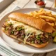 Plato con un Philly cheessteak con papas y pepinillos