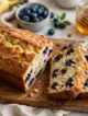 Pan de Plátano con Arándanos: un pan casero húmedo, aromático y lleno de sabor Pan de plátano con arándanos recién horneado sobre una mesa blanca marmoleada