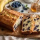 Pan de plátano con arándanos recién horneado sobre una mesa blanca marmoleada
