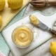 Lemon curd casero servido en un frasco de vidrio con limones frescos y ralladura de limón sobre una superficie de mármol blanco.
