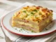 Pastel de papa con jamón cocido y queso fundido recién horneado con superficie gratinada y porción servida.