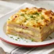 Pastel de papa con jamón cocido y queso fundido recién horneado con superficie gratinada y porción servida.