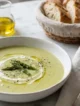 Plato hondo con crema de espárragos decorada con puntas de espárrago, crema y crutones sobre superficie de mármol blanco