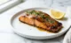Filete de salmón glaseado con miel y ajo, con perejil y ajonjolí, sobre una superficie de mármol blanco