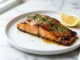 Filete de salmón glaseado con miel y ajo, con perejil y ajonjolí, sobre una superficie de mármol blanco