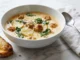 Tazón de sopa de salchicha toscana cremosa con papas y col rizada, con parmesano y pan tostado sobre una superficie de mármol blanco