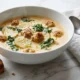 Tazón de sopa de salchicha toscana cremosa con papas y col rizada, con parmesano y pan tostado sobre una superficie de mármol blanco